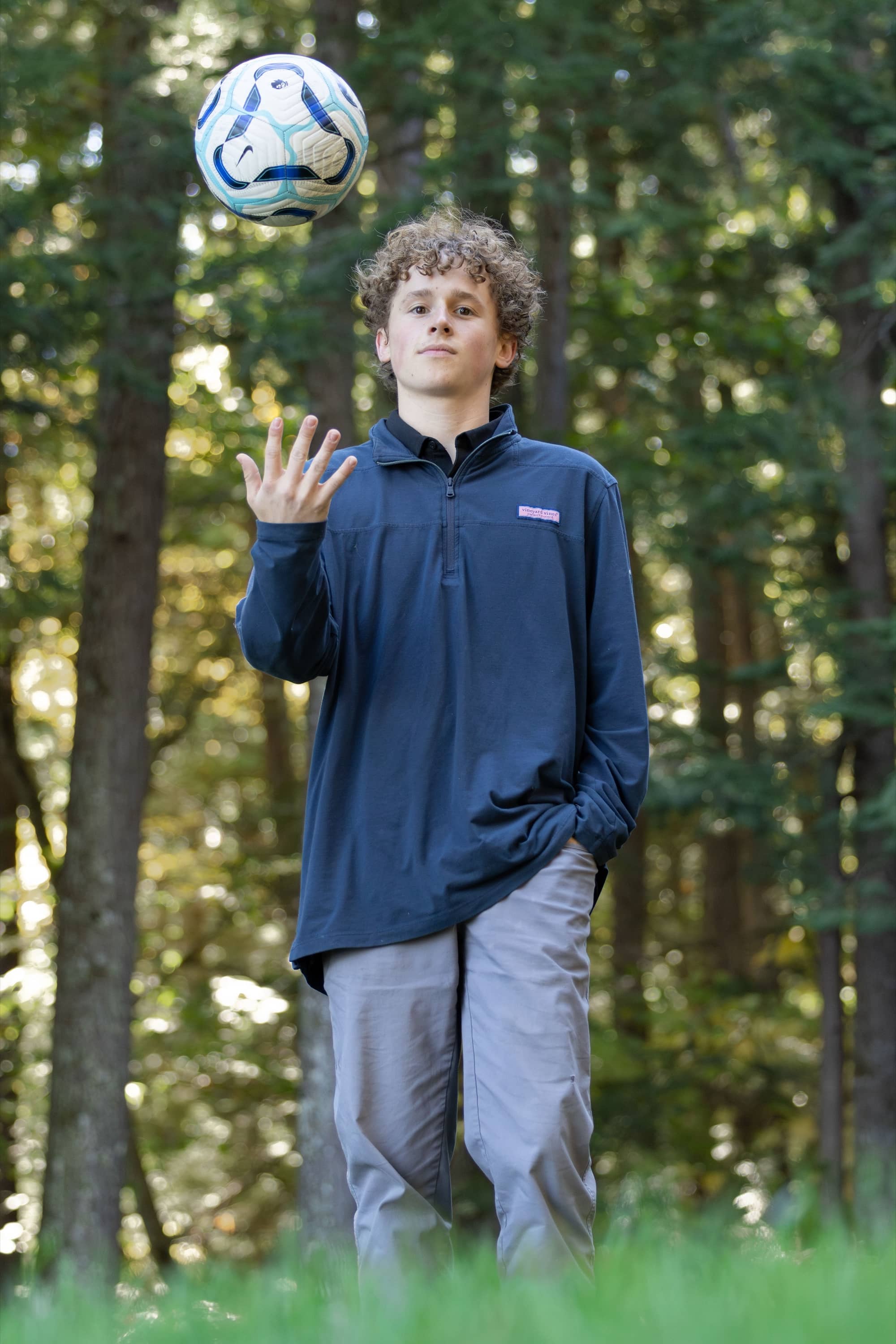 Senior portrait tossing a soccer ball in a wooded setting