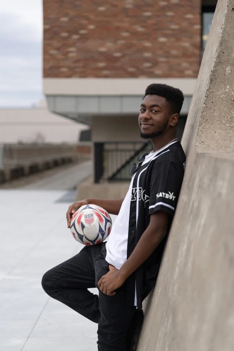 Senior portrait with a soccer ball beside a concrete wall