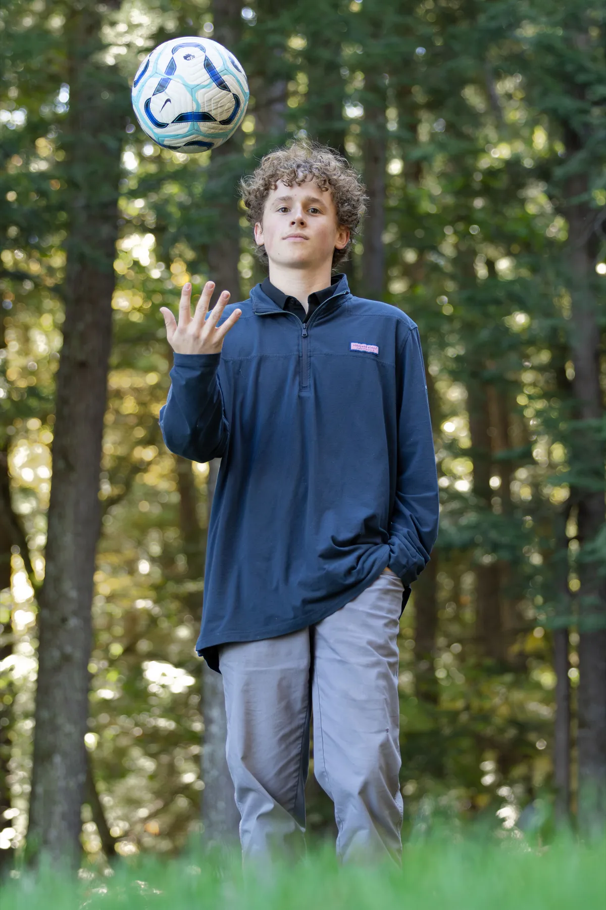 Senior portrait tossing a soccer ball in a wooded setting